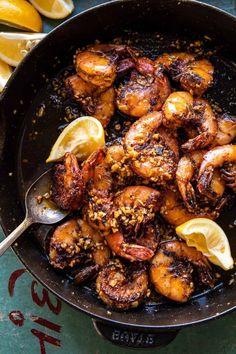 a skillet filled with cooked shrimp and lemon wedges