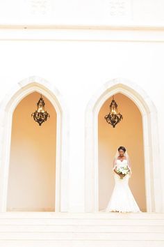 a bride standing in front of two arched doorways holding her bouquet and posing for the camera