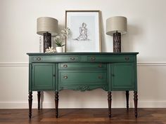 a green dresser with two lamps on top of it next to a painting and lamp shades