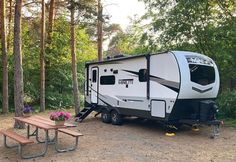 an rv parked in the woods next to a picnic table and bench with flowers on it