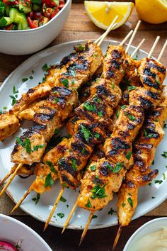 grilled chicken skewers on a plate next to a bowl of salad