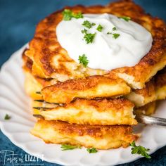 a stack of pancakes with sour cream and parsley on top, sitting on a white plate