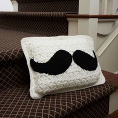 a crocheted pillow with a black mustache on it sitting on the stairs in front of some handrails