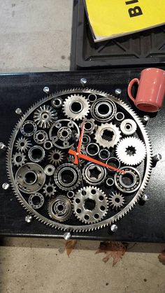 a clock made out of gears with a red coffee cup sitting on top of it