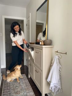 a woman standing in front of a bathroom sink with a dog sitting on the floor