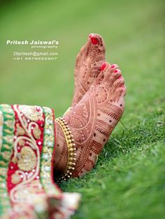 the feet of a woman with henna and jewelry on their feet, in front of green grass