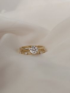 two gold wedding bands with a diamond ring on top of white fabric, close - up