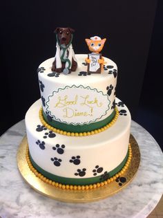 a cake decorated with two dogs and paw prints on the top tier is white, gold, and green