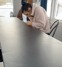 a woman leaning over a table with a remote control in her hand and looking down at it