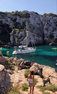 a woman standing on the edge of a cliff looking out at a boat in the water