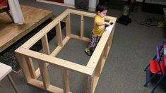 a young boy standing in front of a wooden frame on the floor with chairs around him