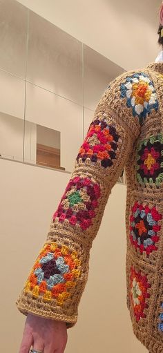 a crocheted jacket is being held by someone's hand