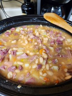 a pot filled with beans and ham on top of a stove next to a wooden spoon