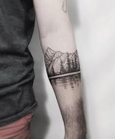 a man's arm with a mountain and pine tree tattoo on the left forearm