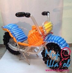 a toy motorcycle made out of balloons on a white sheet with a sign in the background