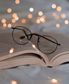 an open book with glasses resting on it's cover and lights in the background