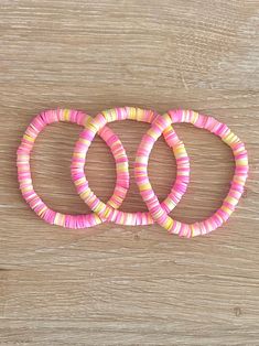 three pink and yellow bracelets sitting on top of a wooden table