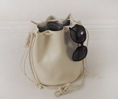 This unique bucket bag features soft, off-white faux (fake) leather, cotton rope shoulder strap, and a drawstring closure. You can tie the cotton rope to wear this bucket bag long or short. Details:-Dimensions when laid flat: 9" length (top to bottom), 7.5" diameter round bottom-Shoulder strap measures approx. 45-50" total-Soft, off-white faux (fake) leather-Solid light color interior lining-No internal pocketBecause each bag is made by hand, the measurement is approximate and may vary slightly Color Interior, Vintage Backpacks, Drawstring Bucket Bag, Leather Bucket Bag, Leather Bucket, Fabric Bags, One Bag, Cotton Rope, Sewing Bag