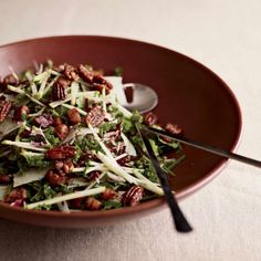 a salad in a brown bowl with pecans and shredded cheese on top, sitting on a table