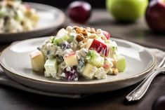 a salad with apples, grapes and nuts on a white plate next to silverware