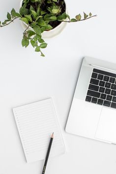 an open laptop computer sitting on top of a white desk next to a pen and paper