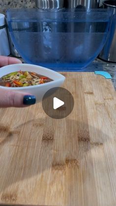 a person holding a bowl of food on top of a wooden cutting board