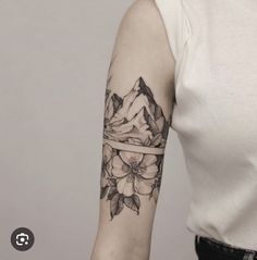 a woman's arm with flowers on it and mountains in the distance behind her