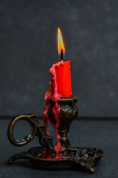 a red candle is lit on top of an ornate stand with a key in the middle