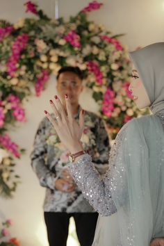 a man standing next to a woman in front of a floral wall with pink flowers