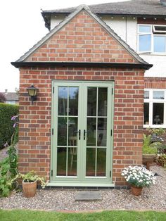 a brick building with green doors and windows in the front yard, surrounded by potted plants