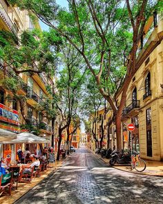 an empty street with tables and chairs on the side, surrounded by trees in front of buildings