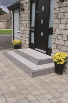 two planters with yellow flowers are on the front steps of a brick building, near a black door