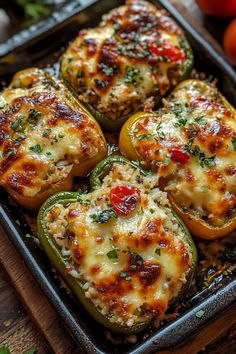 four stuffed peppers in a baking pan with cheese and herbs on top, ready to be eaten