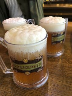 two mugs filled with beer sitting on top of a wooden table