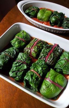 two white dishes filled with green vegetables on top of a wooden table