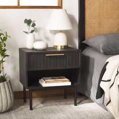 a nightstand with a book on it next to a bed and plant in the corner