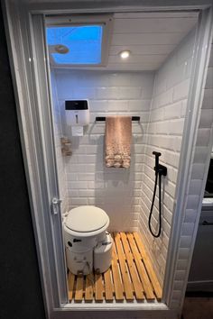 a small bathroom with a toilet and shower in the corner, next to a wooden pallet floor