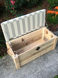 an empty wooden box sitting on top of a cement ground next to flowers and bushes