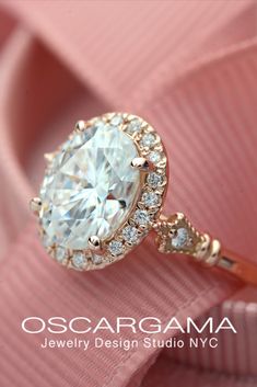 an engagement ring with a large white diamond surrounded by small round diamonds on pink fabric