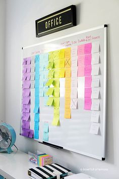 a bulletin board with sticky notes attached to it and a fan on the wall behind it