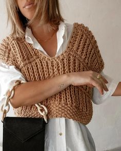 a woman wearing a knitted vest holding a black purse