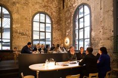 a group of people sitting around a table in front of two large windows with lots of windows