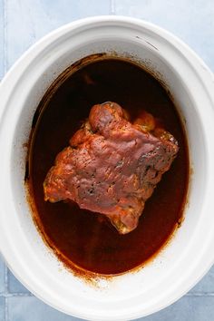 a white bowl filled with meat and sauce on top of a blue tablecloth covered floor