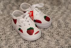 a pair of white shoes with strawberries painted on them sitting on a carpeted surface