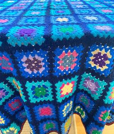 a blue crocheted tablecloth with multicolored flowers on it, sitting on a wooden surface