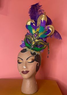 "Get ready to party on the parade route as the floats wheel on by. You will be sure to get the best loot, from beads to shoes, in this showstopping headpiece band.  A green fascinator base, with a green ribbon wrapped thin metal headband, trimmed with studded gold trim supports a Mardi Gras masquerade mask with a large central rhinestone and three dangly sequin and stone \"tassels\". Behind the mask is a large gold fleur de lis and purple ostrich plumes. The back features a wired ribbon bow with tulle.  Due to the tilt of the piece, I recommend wearing with a few bobby pins. At least one on each side, and one in the back over the edge to \"anchor\" it in place, so it stays perfectly placed while you shimmy on the parade route to the best bands.  Support local Louisiana artists this Carniva Mardi Gras Headpiece, Witch Brooms, Homecoming 2024, Halloween Witch Brooms, Mardi Gras Masquerade, Green Fascinator, Behind The Mask, Mardi Gras Costumes, Mardi Gras Parade