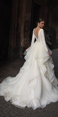 a woman in a white wedding dress is walking down the street with her back to the camera