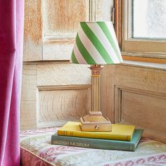 a lamp sitting on top of a bed next to two books and a pink curtain