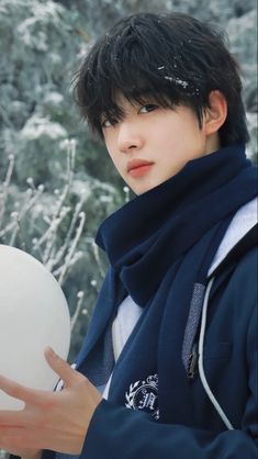 a young man holding a white frisbee in front of snow covered trees and bushes