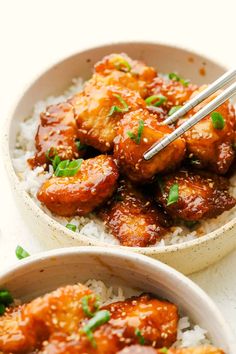 two bowls filled with chicken and rice on top of a white countertop next to chopsticks